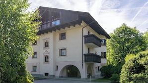 A multi-story building with a balcony on the second floor, a central entrance with an archway, and a surrounding garden.