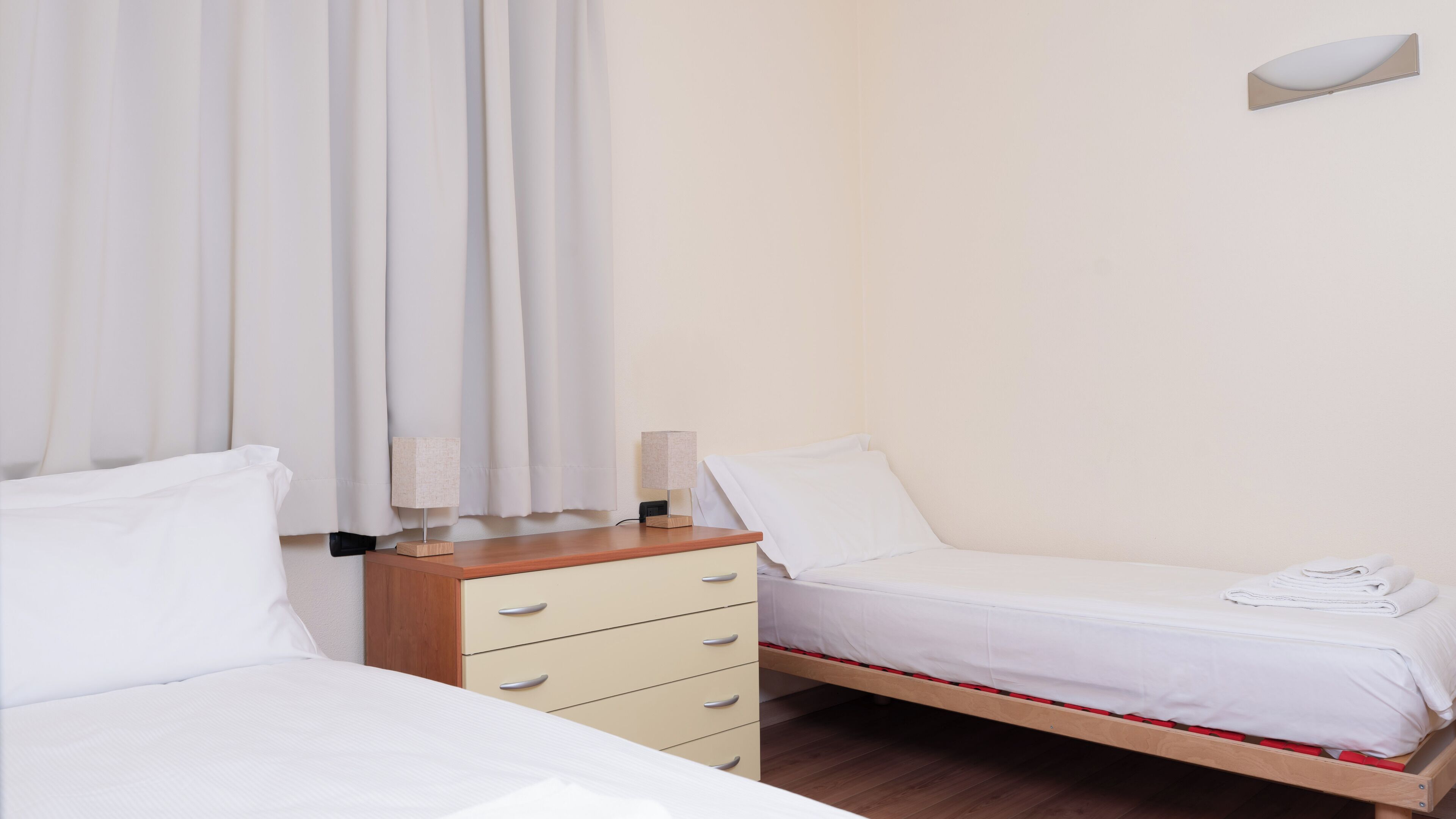 Una camera da letto con due letti, un comodino in legno, una lampada e un comò.