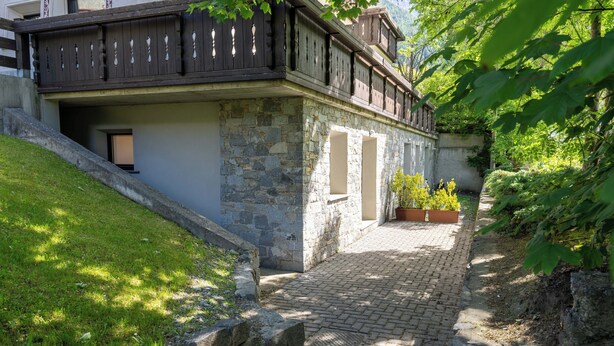 A stone building with a wooden balcony, a paved pathway, and potted plants.