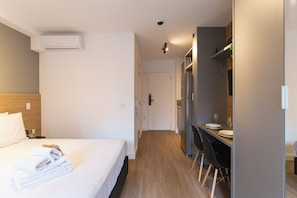 A hotel room with a neatly made bed, a desk with chairs, and a dining area. - My One Bela Vista NR (Sao Paulo)