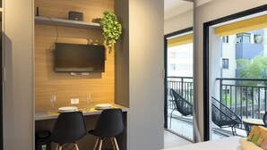 A modern hotel room with a bed, a desk with two chairs, a TV, and a balcony with chairs. - My One Bela Vista NR (Sao Paulo)