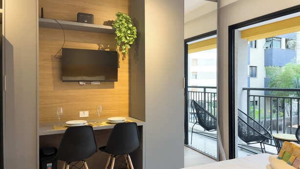 Habitación de hotel moderna con cama, escritorio con dos sillas, televisor y balcón con sillones.
