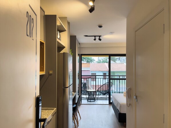 A modern apartment with a kitchen, a balcony with a chair, and a bedroom with a bed and a phone. - My One Bela Vista NR (Sao Paulo)