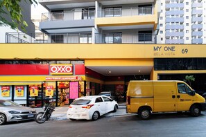 Um edifício com fachada amarela, um letreiro com 'My One Bela Vista 69' e uma vitrine com a marca 'OXO'.