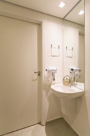 Casa de banho com uma pia branca, um espelho e dois secadores de cabelo fixados na parede.