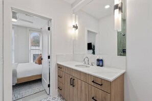 Ein modernes Badezimmer mit einem weißen Waschtisch, einem großen Spiegel und einer Duschkabine.