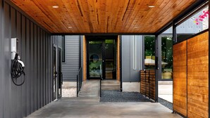 Una entrada moderna de edificio con piso de concreto, techo de madera y paredes de metal y madera.
