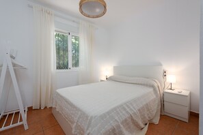 Quarto com cama, mesa de cabeceira, abajur, janela com cortinas e guarda-roupa branco.