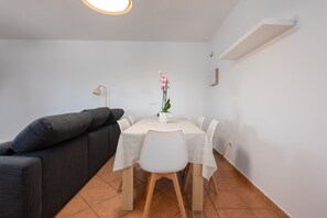 Uma sala de jantar com uma mesa posta para quatro, um sofá cinzento, uma orquídea em vaso e uma luminária pendente.