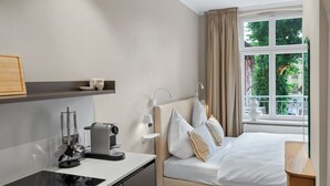 A modern hotel room with a bed, bedside table, and a window with a view of greenery. - Balcony apartment 12 Korn (Unknown)