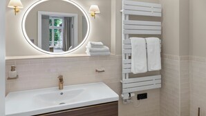 A bathroom with a white sink, wooden vanity, a towel rack with towels, and a mirror with a light. - Balcony apartment 12 Korn (Unknown)