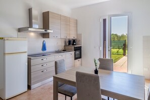Une cuisine moderne avec un coin repas, un four encastré et une vue sur le jardin par la porte.