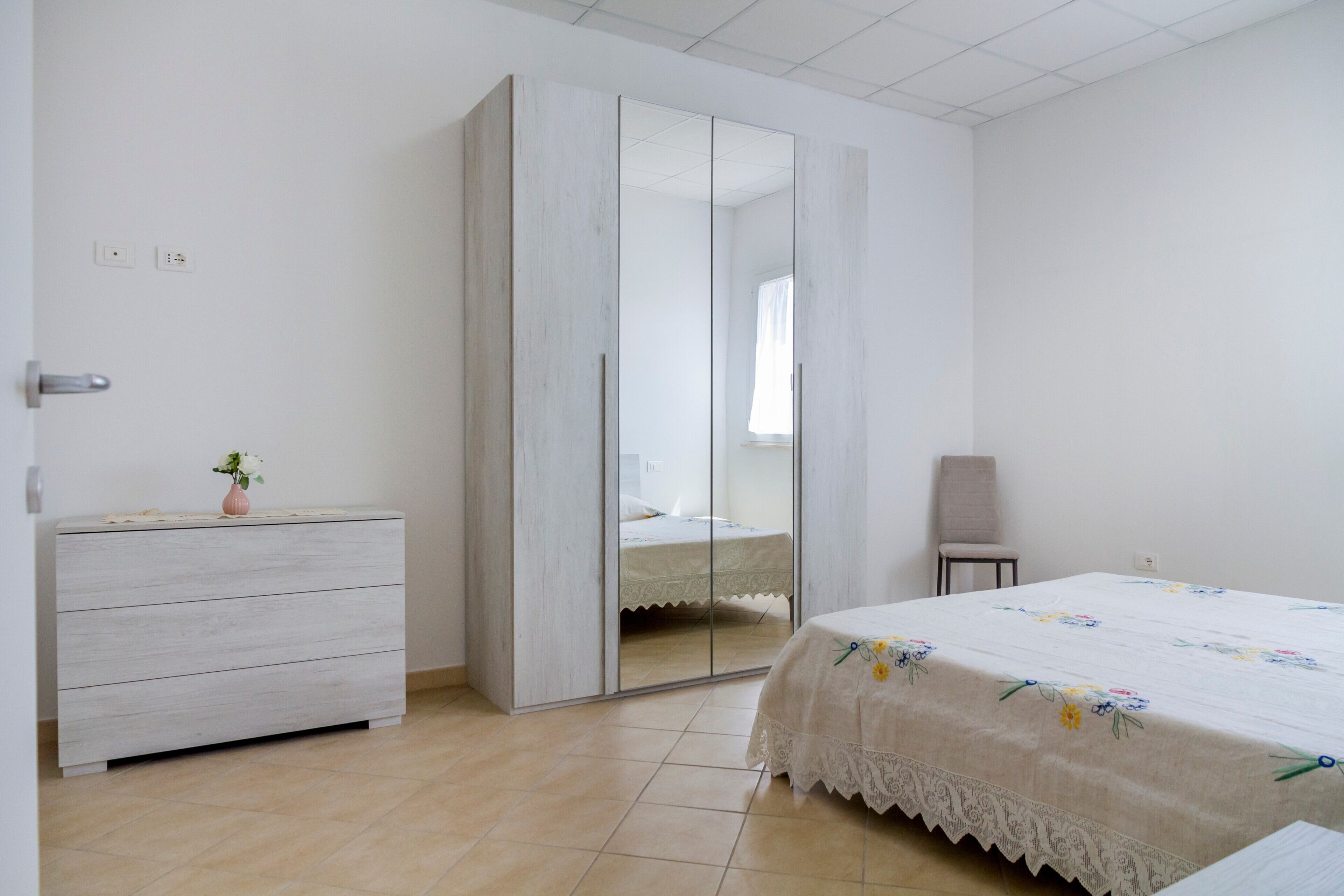 Un dormitorio con cama, cómoda, silla y armario con espejo.