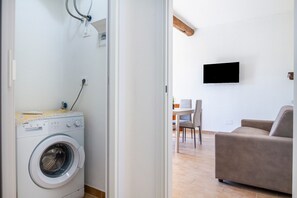 Un espace buanderie avec un lave-linge, un coin repas avec une table et des chaises, et un téléviseur à écran plat fixé au mur.