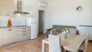 A modern kitchen with a built-in oven, a dining area with a table and chairs, and a grey sofa.