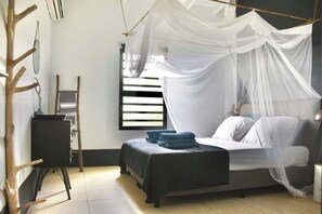 Una habitación con una cama bajo un dosel, una pequeña mesa con una silla y una ventana con persianas.