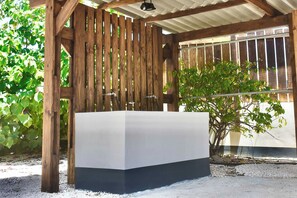 Un área de estar al aire libre techada, con una pérgola de madera, una mesa blanca y una planta en maceta.