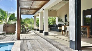 A covered outdoor area with a pool, wooden deck, and seating arrangements.
