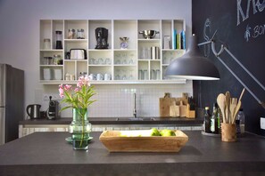 Una cocina moderna con una lámpara colgante negra, un florero con flores y una tabla de cortar de madera con manzanas.
