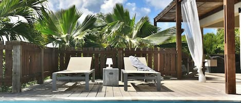 A poolside area with two lounge chairs and a wooden deck.