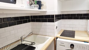 A compact kitchen with a washing machine, a sink with a drying rack, and a countertop with a microwave and various kitchen items.