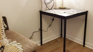 A corner table with a lamp, a power cord, and a piece of artwork on the wall.