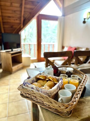 A breakfast tray with bread, juice, and a mug on a table in a room with wooden furniture and a TV. - Apart Hotel Rucaleufú (San Martín de los Andes)