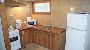 A kitchen with wooden cabinets, a white refrigerator, a microwave, a stove, and a sink.