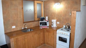 A compact kitchen with wooden cabinets, a stainless steel sink, a microwave, a coffee maker, and a gas stove.
