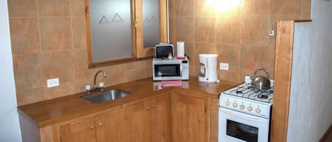 Cocina compacta con armarios de madera, un lavamanos de acero inoxidable, microondas, cafetera y cocina a gas.