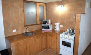 A compact kitchen with wooden cabinets, a stainless steel sink, a microwave, a coffee maker, and a gas stove. - Apart Hotel Rucaleufú (San Martín de los Andes)
