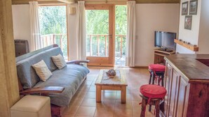 A cozy living room with a sofa, a coffee table, and a TV. There is a balcony with a wooden railing and a door leading outside. - Apart Hotel Rucaleufú (San Martín de los Andes)