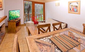 A living room with a television, wooden furniture, a glass coffee table, and a view through a large window. - Apart Hotel Rucaleufú (San Martín de los Andes)