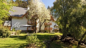 A two-story building with a white exterior, wooden balconies, and outdoor seating areas. - Apart Hotel Rucaleufú (San Martín de los Andes)