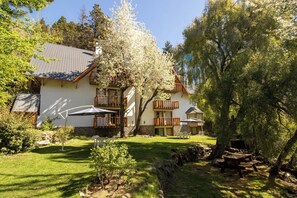 A two-story building with a white exterior, wooden balconies, and outdoor seating areas. - Apart Hotel Rucaleufú (San Martín de los Andes)