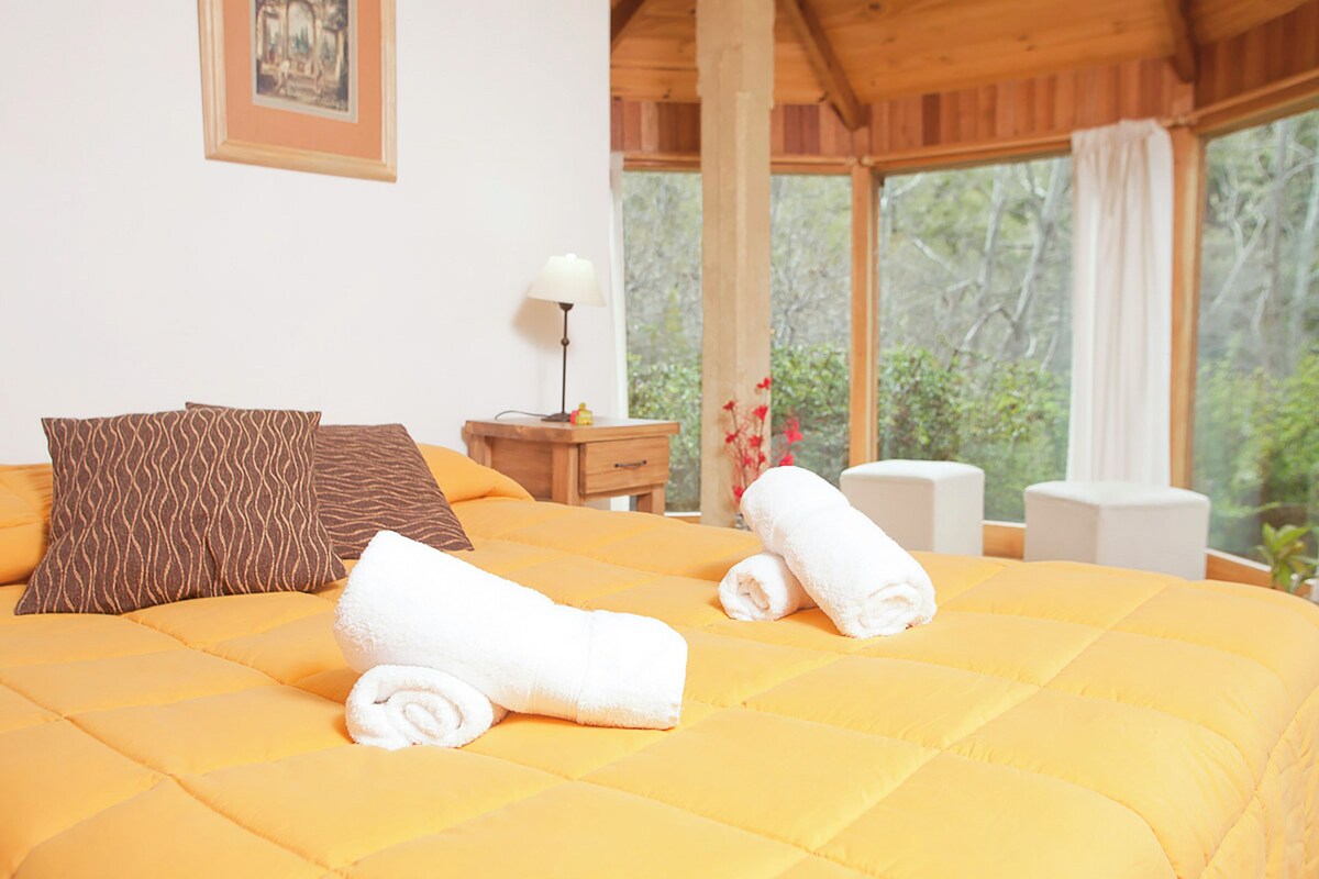 A bed with a yellow quilt, two rolled towels, and patterned pillows.