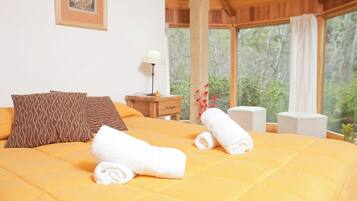 A bed with a yellow quilt, two rolled towels, and patterned pillows.