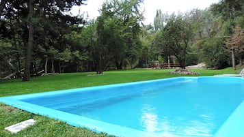 Una piscina rectangular con revestimiento azul, rodeada por un césped y árboles.