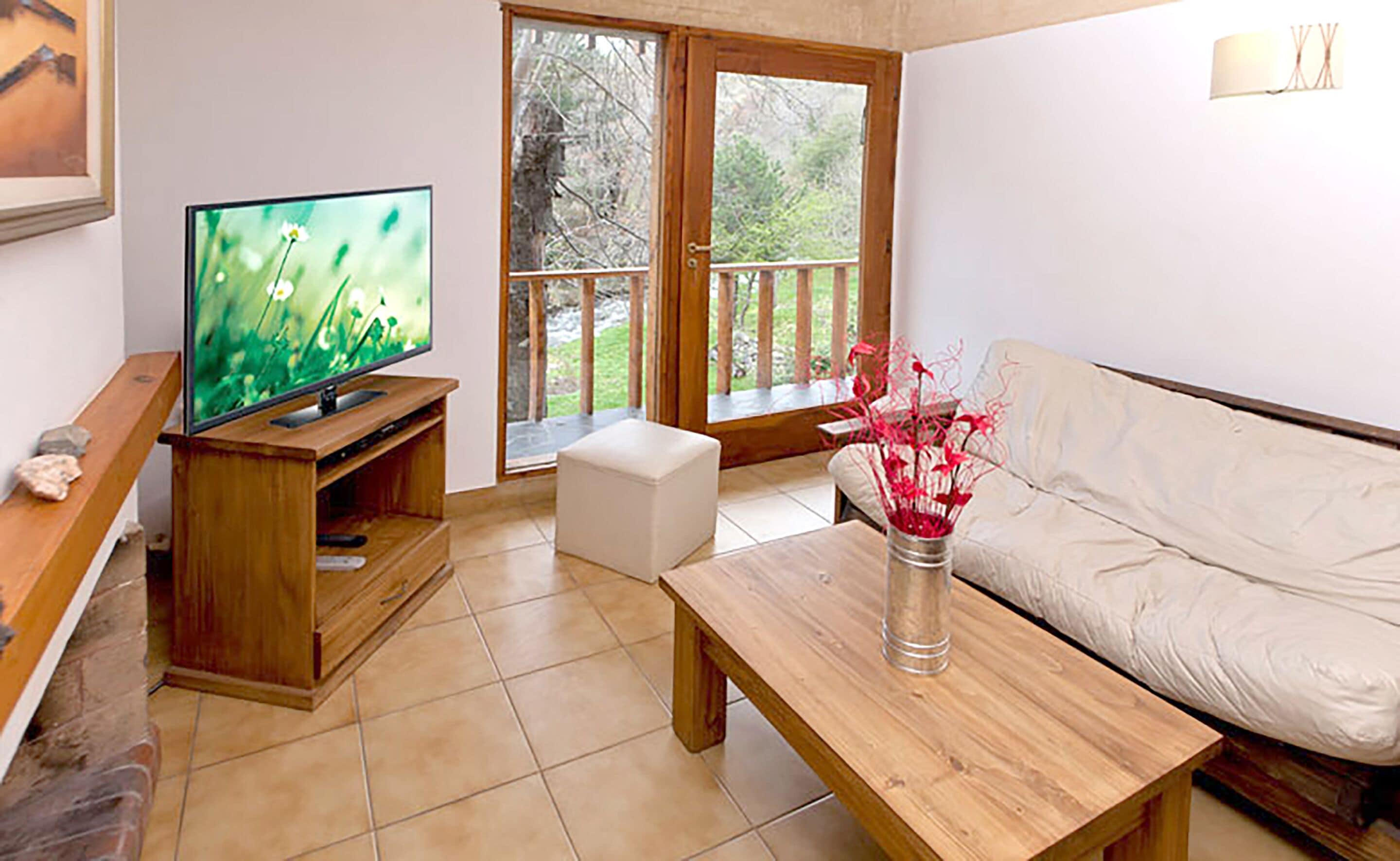 A living room with a TV, a white sofa, a wooden coffee table, and a glass vase with flowers.