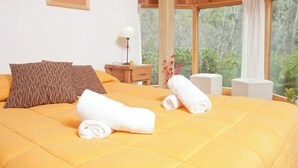 Una cama con un edredón amarillo, dos toallas enrolladas y almohadas estampadas.