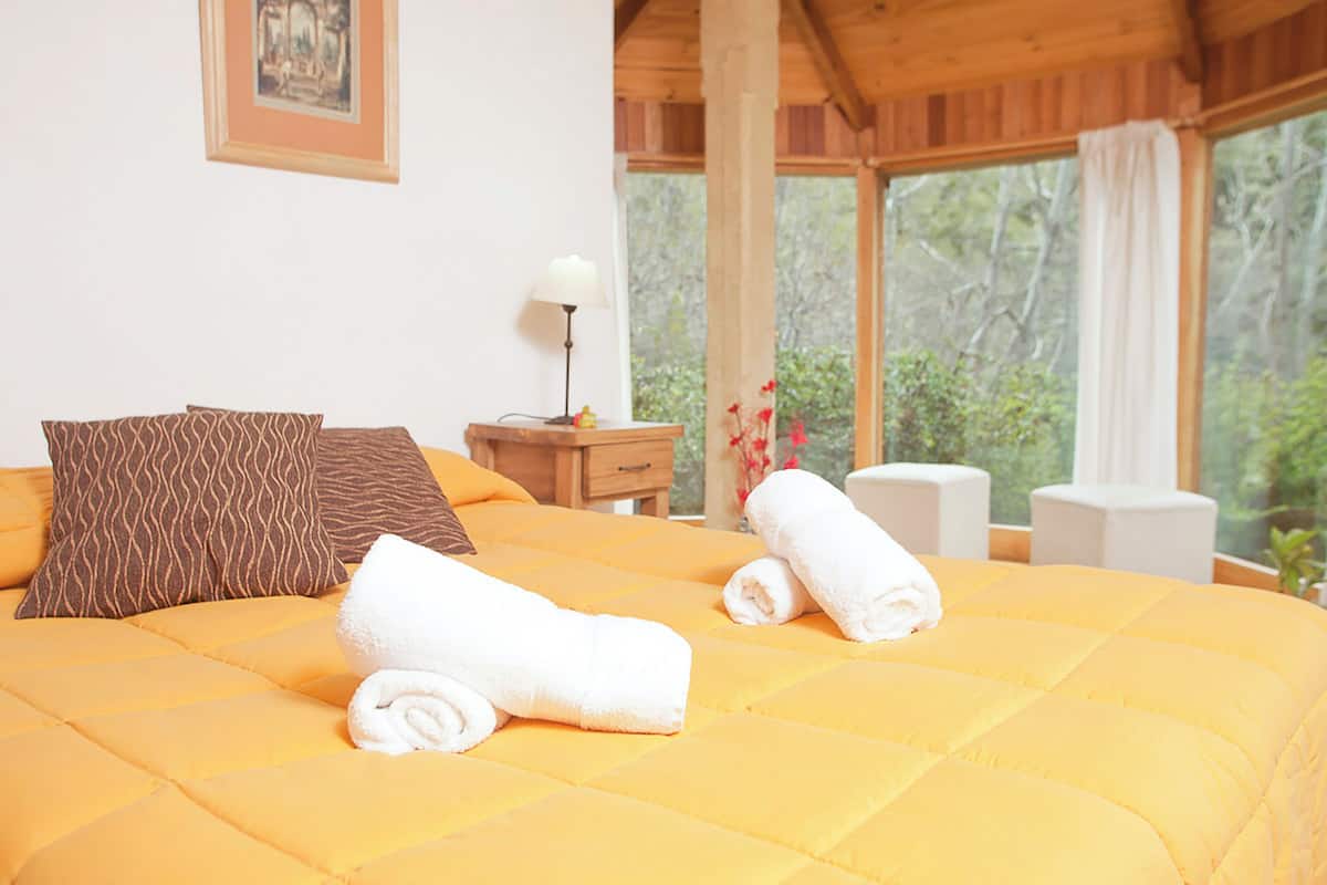 A bed with a yellow quilt, two rolled towels, and patterned pillows.