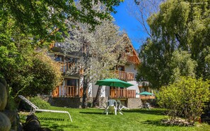 A multi-story building with balconies, a stone facade, and a well-maintained lawn. - Apart Hotel Rucaleufú (San Martín de los Andes)