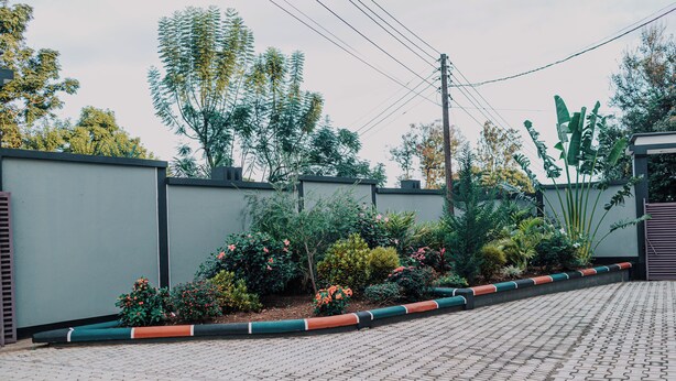 A paved walkway with a low wall and a variety of plants and shrubs. - St. Benedict House (Moshi)