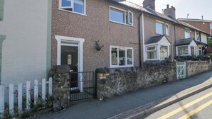 A row of terraced houses with a stone wall, a white picket fence, and a street with yellow double lines. - Bryn Hyfryd (Conwy)