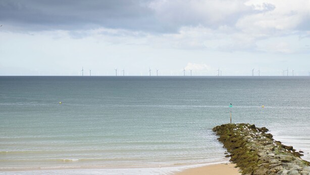 A beach with a rocky breakwater and a view of wind turbines in the distance. - Bryn Hyfryd (Conwy)