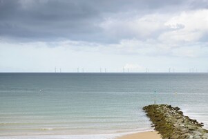 Una playa con un rompeolas rocoso y una vista de aerogeneradores a lo lejos.