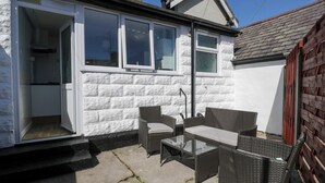 A small house with a patio area featuring wicker furniture and a glass table. - Bryn Hyfryd (Conwy)