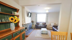 A living room with a fireplace, a sofa, a dining table with chairs, and a TV mounted on the wall. - Bryn Hyfryd (Conwy)