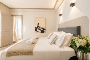 A hotel room with a bed, a painting, a vase with flowers, and a door leading to another room. - 1539 Belles Feuilles (Paris)
