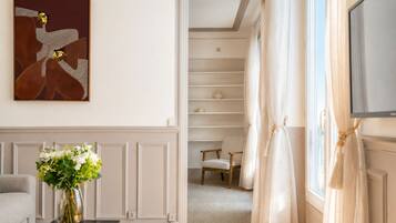 Una sala de estar moderna con un sofá, una mesa de centro con un florero, un cuadro en la pared y vistas a un dormitorio a través de un vano.